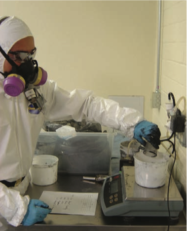 A worker wearing a respirator, lab coat, and gloves while weighing carbon nanotubes