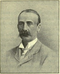 Photographie en noir et blanc en buste d'un homme moustachu et dégarni.
