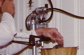 Lapping tool on a spindle below the lens, and mounting tool on a second spindle (swung out) uses pitch to hold the lens shown with its concave side down