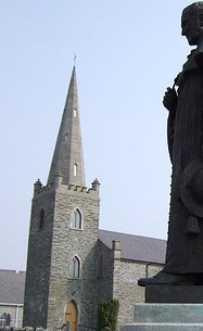 The ashlar spire seen beyond statue commemorating Cardinal Patrick O'Donnell in St Eunan's Cathedral grounds Conwal Parish Church spire Statue.jpg