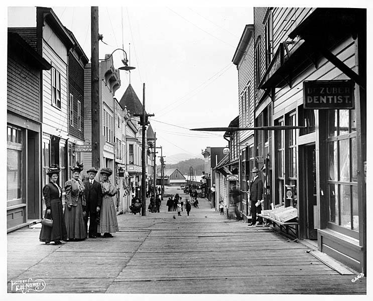 File:Ketchikan board street, with people and storefronts, including signs for Dr Zuber, Dentist, Emerald Saloon, and the Ketchikan (NOWELL 226).jpeg