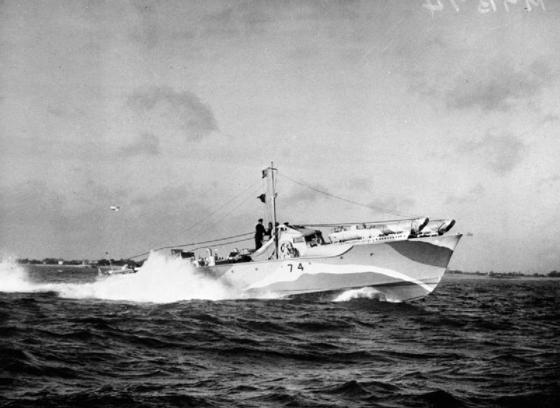 Ship speeding at sea with a white bow wave; land can be seen in the background