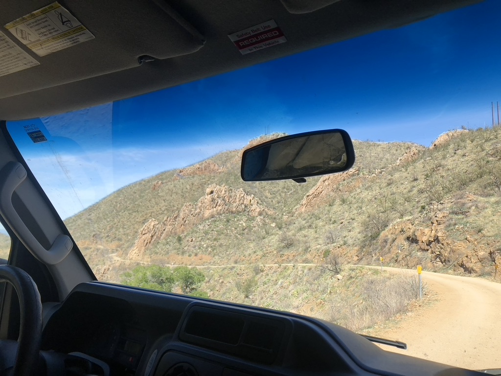 A dirt road in a canyon with no guardrail seen through the front window of a van