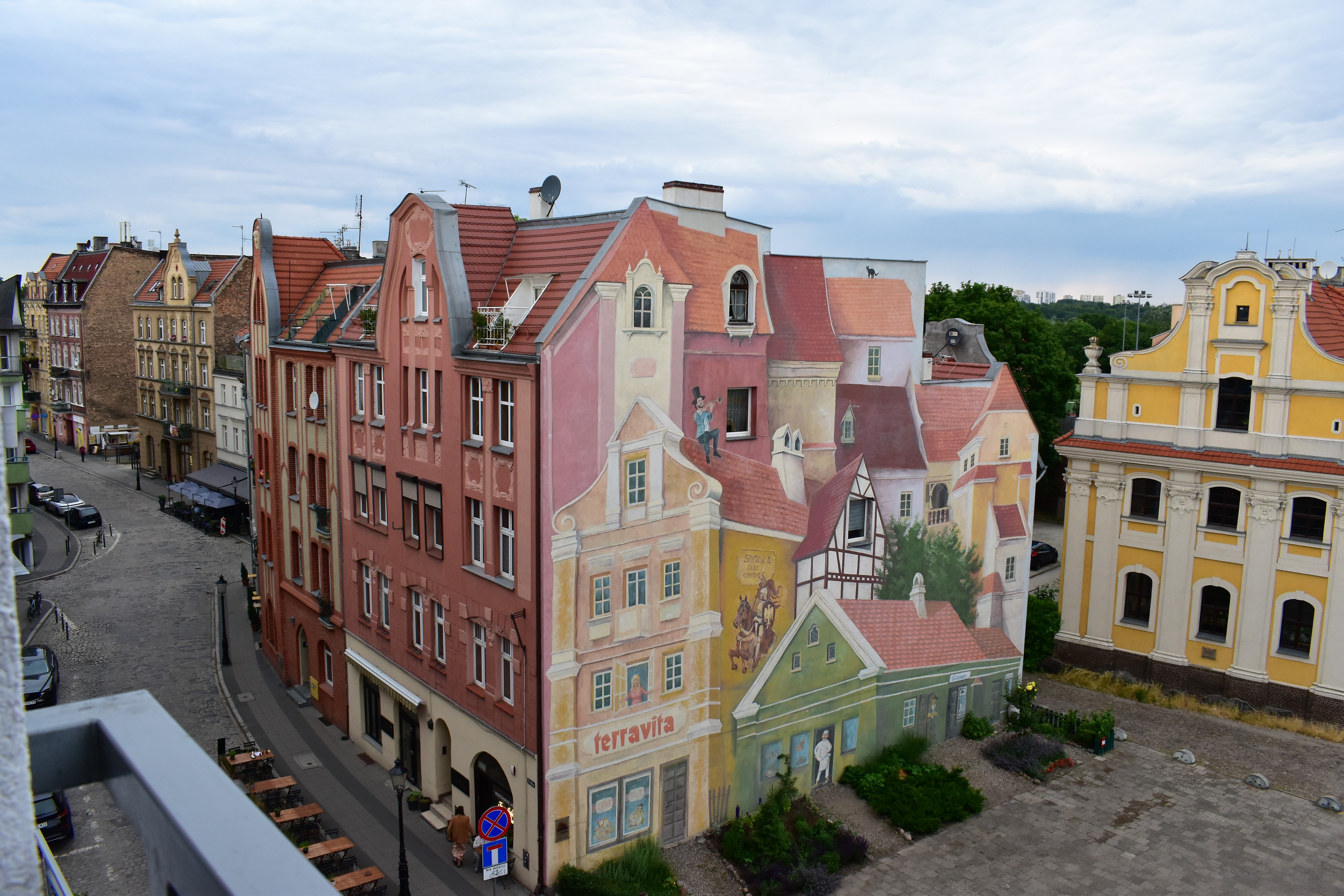 Widok na ulicę Śródecką (po lewej) i ścianę kamienicy na Rynku Śródeckim w Poznaniu z iluzjonistycznym obrazem miejskiej sielanki.
