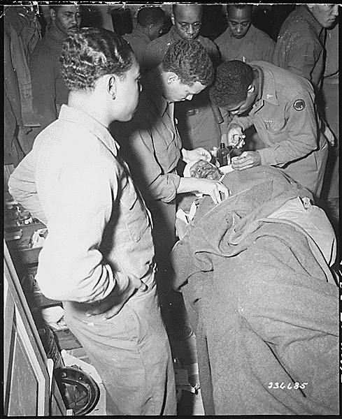 File:"Capt. Ezekia Smith, 370th Inf. Regt., 92nd Div., receives treatment at the 317th Collecting Station, for shell fragments in face and shoulders suffered near Querceta, Italy. Here, surgeon stitches the wound. Fifth(...) - NARA - 531332.gif