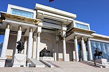 A large glass and stone-fronted building, with three large statues placed around external steps