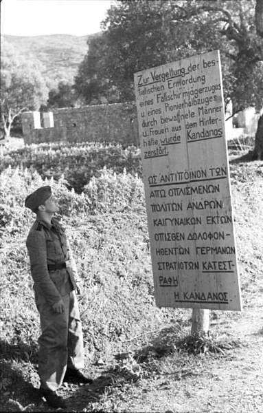 A German soldier in front of a sign erected after the razing of Kandanos. The sign reads: "Kandanos was destroyed in retaliation for the bestial ambus