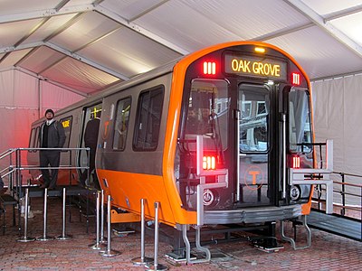A subway rail car prototype with orange trim sits on a raised platform a tent with stairs to one entrance and a ramp to the opposite entrance