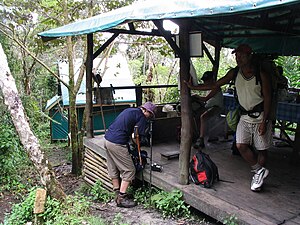 Un grupo de personas se prepara para salir cerca del refugio de comidas, con un bungalow al fondo.