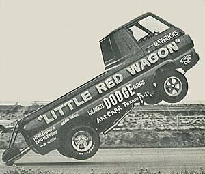 A black and white photograph of the Little Red Wagon performing a wheelstand during a race.
