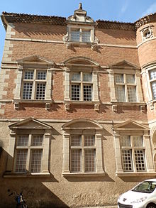 zemin katta üç pencereli ve taş duvarlı, üst katta üç pencereli, tuğla duvar üzerinde öncekilerle aynı hizada olan bir evin renkli fotoğrafı.