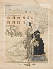 A man and a woman in Victorian-era clothing walk arm-in-arm along a street. The woman carries a handbag that advertises a local department store.