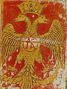 Ο δικέφαλος αετός με το μονόγραμμα (συμπίλημα) των Παλαιολόγων στο κέντρο, έμβλημα της Δυναστείας και της Βυζαντινής Αυτοκρατορίας. Τοιχογραφία του 14ου αιώνα σε ναό.