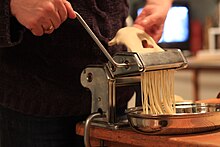 Fresh spaghetti being prepared using a pasta machine