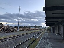 Wellsford railway station on the North Auckland Line in 2018, with logs to be loaded onto a train. Wellsford railway.jpg