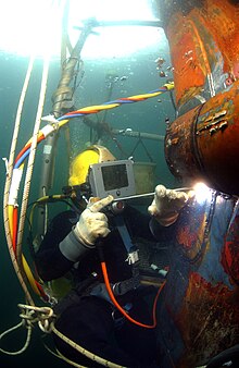 Водолаз в водолазном шлеме сваривает ремонтную заплату на подводной лодке