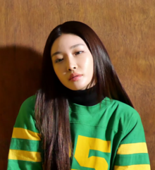 Chungha looks forward in a green shirt against a brown background