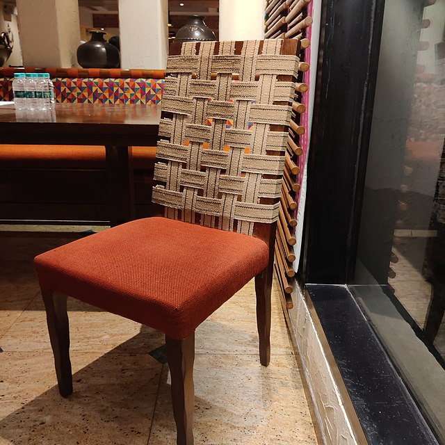 A wooden chair with a cotton niwar webbed back