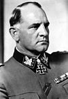 A black-and-white photograph of a man in semi profile wearing a military uniform and neck order, in shape of an Iron Cross. He has short, thinning hair and a determined facial expression.