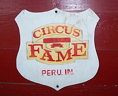 Emblema del Salón de la fama del circo, un escudo blanco sobre fondo rojo con las palabras "Circus Hall of Fame, Peru, In." escritas sobre etiquetas doradas.