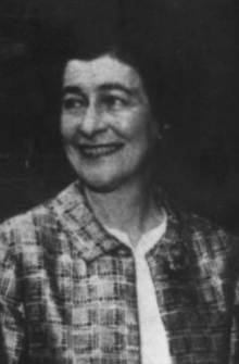 A smiling white woman with dark hair, wearing a print jacket over a white blouse