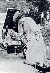 Foto de una mujer frente a un automóvil, con una mano en el capó del motor.