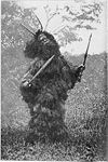 Vestafrikansk fetisj-trollmann med horn, tremaske, spyd, sverd og en drakt av palmeblader. Foto fra boka Fetishism in West Africa: Forty Years' Observations of Native Customs and Superstitions fra 1904.