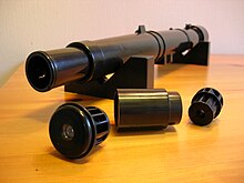 At the front, left: The four-lens main eyepiece. Middle: Barlow tube. Right: The two lens auxiliary eyepiece. Background: The focus tube and main telescope tube containing the achromatic doublet objective lens. Galileoscope3.jpg