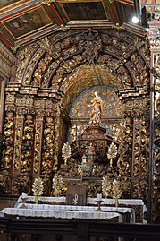 Photographie d'une statue de Marie surplombant un autel et entouré d'un retable monumental à colonnes torsadées.