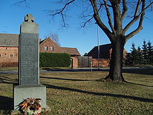 Kriegerdenkmal, im Hintergrund ein denkmalgeschütztes Gehöft