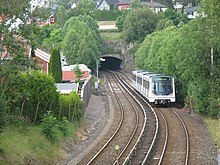 Double-track jalur kereta bawah tengah dari gambar setelah muncul dari terowongan. Garis ini dikelilingi oleh rumah-rumah dan pohon-pohon, dan putih, tiga mobil kereta setengah jalan ke bawah garis di sisi kanan.