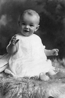 Monroe as an infant, wearing a white dress and sitting on a sheepskin rug