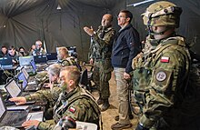 Army Secretary Mark Esper visits with Polish soldiers training with American troops in Germany in 2018. Esper would later reactivate the Army's heavy V Corps in Poland as NATO improved its readiness against Russian revanchism. Mark Esper visits with Polish soldiers training with American troops in Germany in 2018. Esper would later reactivate the Army's V Corps in Poland as DOD increasingly faced off against Russia.jpg