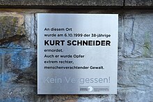 Silberne Gedenktafel mit schwarzer Schrift befestigt auf einer Steinmauer. Darauf steht: "An diesem Ort wurde am 6.10.1999 der 38-jährige Kurt Schneider ermordet. Auch er wurde Opfer extrem rechter, menschenverachtender Gewalt. Kein Vergessen!"