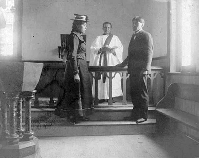 Young woman and young man standing at a church altar with a priest