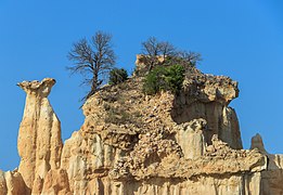 Питоны рассыпчатой ​​белой земли, увенчанные камнями и кустарниками, возвышаются в небо