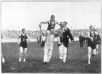 černobílá fotografie: muži běží na stadionu;  jeden z nich je nesen vítězně