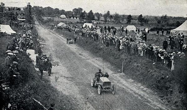 1903 Gordon Bennett Trophy. René de Knyff, driving his Panhard to second place, passes Alexander Winton repairing the Winton Bullet 2 on the first lap