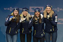 Cuatro esquiadores de fondo, enfrentados, presentando sus medallas a los fotógrafos.