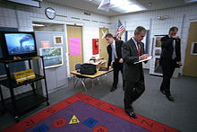 President Bush leaves his Booker elementary classroom visit and enters his staff's holding room as the television plays footage of the burning towers. George W. Bush with burning towers on television.jpg