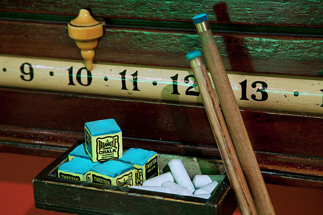 A sliding scoreboard, some blocks of cue-tip chalk, white chalk-board chalk, and two cue sticks