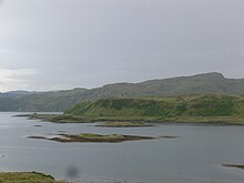 The north of Torsa with visible raised beach line below the cliffs. Sgeir a' Bodaich is at centre and Glas Eilean between there and Torsa. The heights of Dùn Crutagain on the mainland of Scotland are beyond.