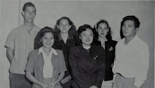 Photograph of a group of four young women standing between two young men.