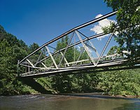 A metal-frame bridge over a broad stream in a forest