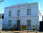 Double storey, 3-bay house with stepped-up parapet decorated with scrolls and two string courses with two rectangular and one round vent between. Corner quoins and moulded plaster surrounds to openings. Small 6 x 6 sashes to first floor. Large 6 x 6 sash Type of site: House Current use: House. 78 Stockenstrom Street, Worcester, South Africa.jpg