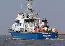 A white colored boat with a blue hull from the back.