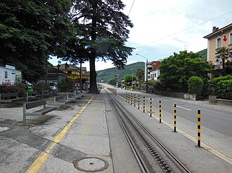 Looking south along Capolago's main street, with the railway station (in yellow) and the track of Monte Generoso railway Capolago-Riva San Vitale railway station 04.jpg