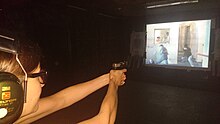 A woman trains real-life defensive gun use scenarios with live ammunition at a video shooting range in Prague, Czech Republic. Defensive gun use training - Prague Cech Republic.jpg
