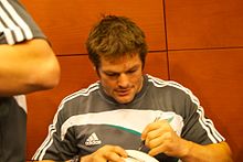 McCaw podpisuje lewą ręką piłkę do rugby prezentowaną przez kibica.