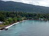 View of Halmahera island, a dark sand beach with small piers in front of a low forested area with forested hills in the background